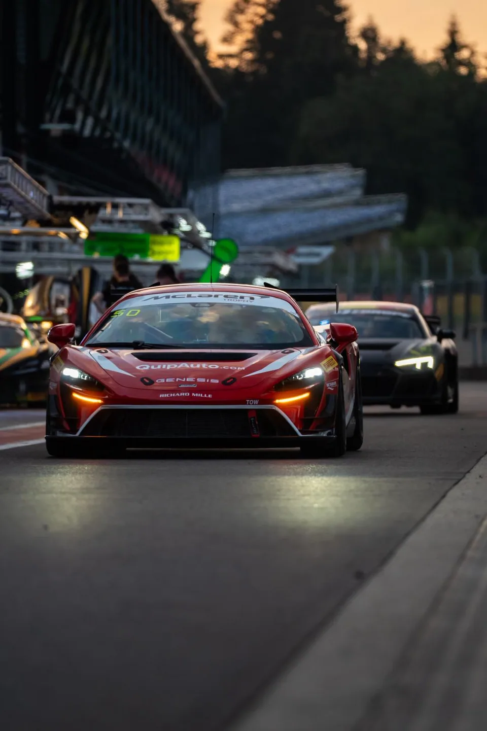 Voitures de course alignées de nuit sur la piste, feux avant allumés