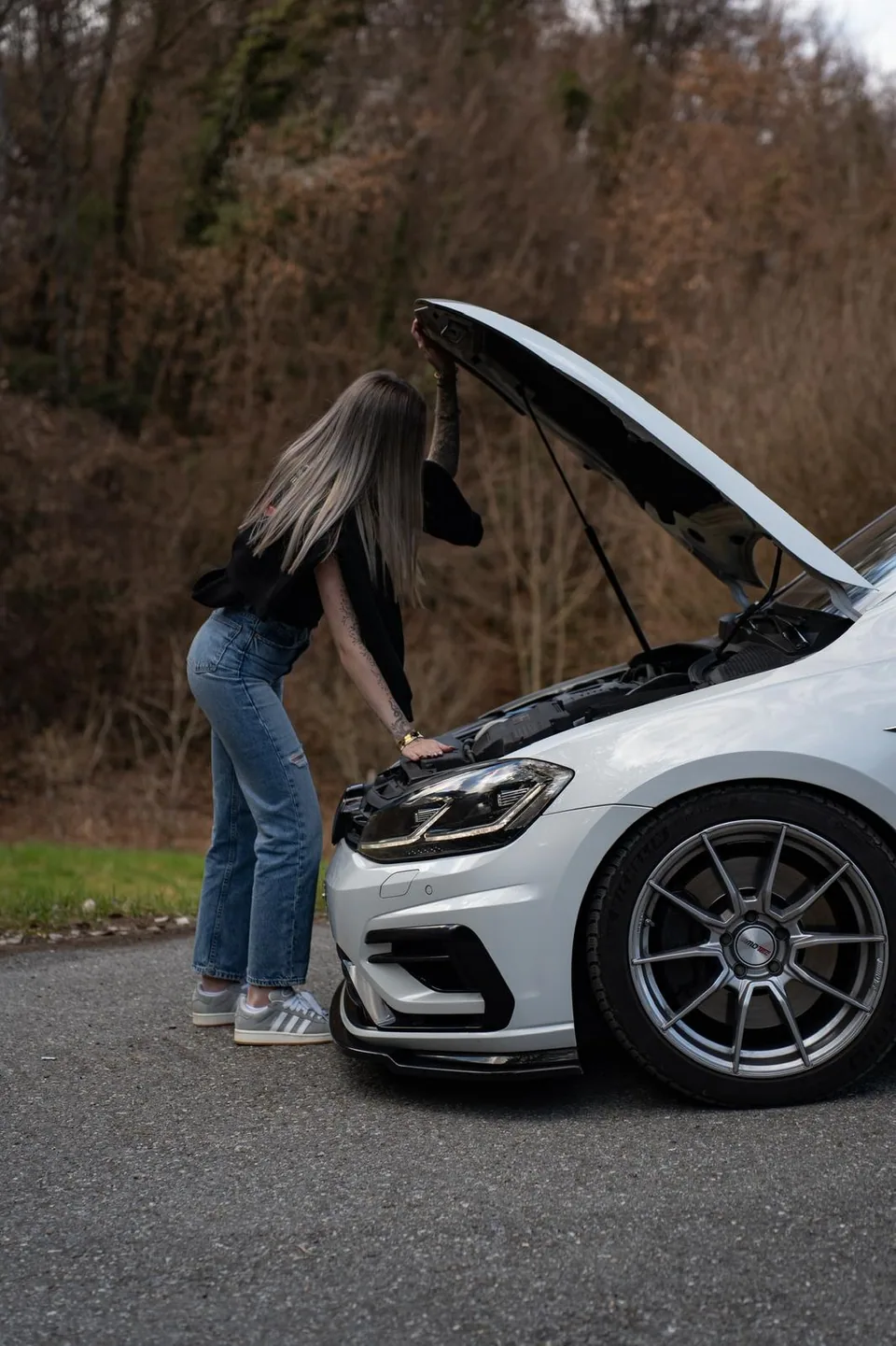 Personne ouvrant le capot d'une Volkswagen Golf R blanche, vue de profil