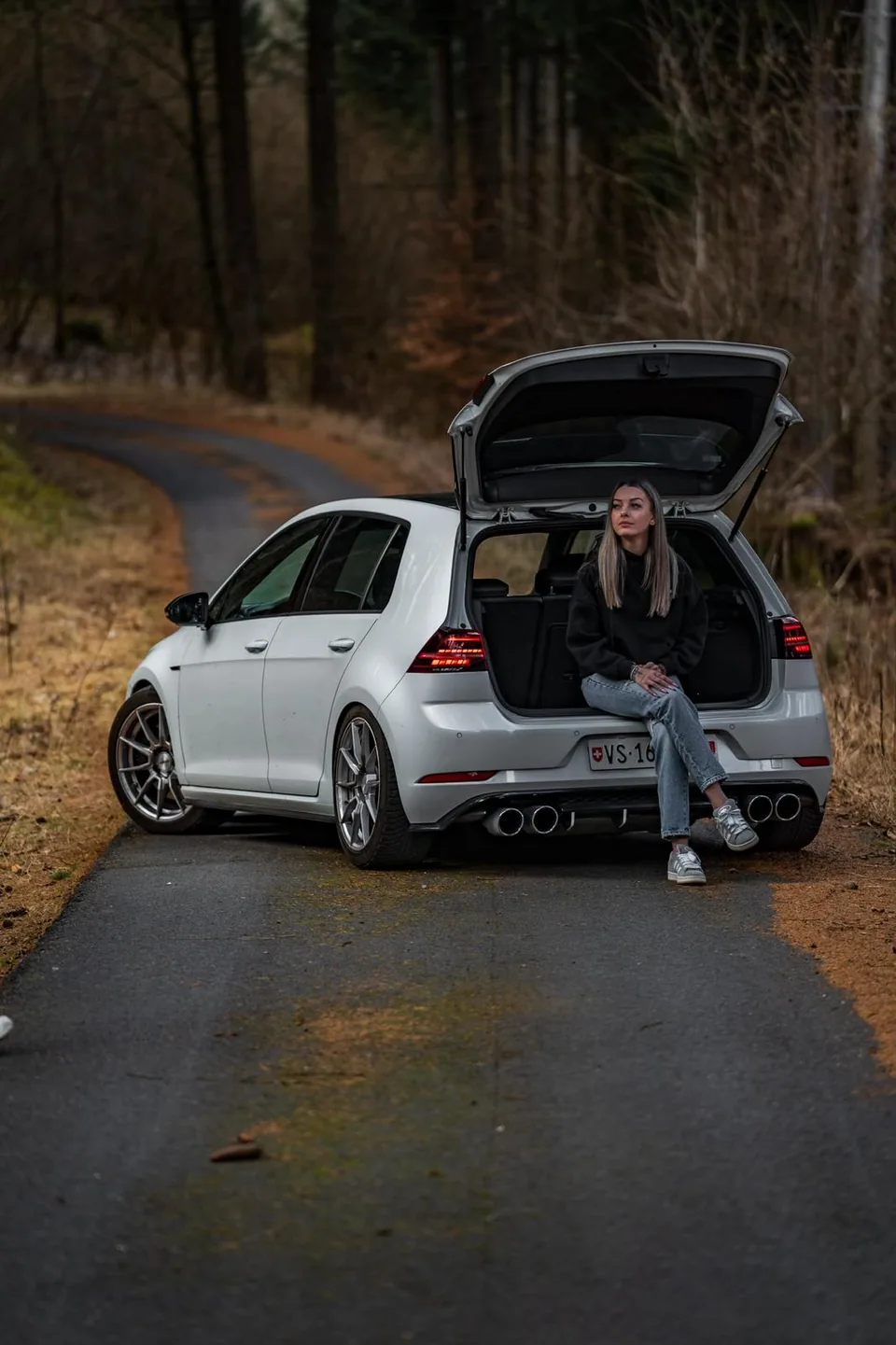 Volkswagen Golf R blanche hayon ouvert sur une route en lacet, une personne assise dans le coffre