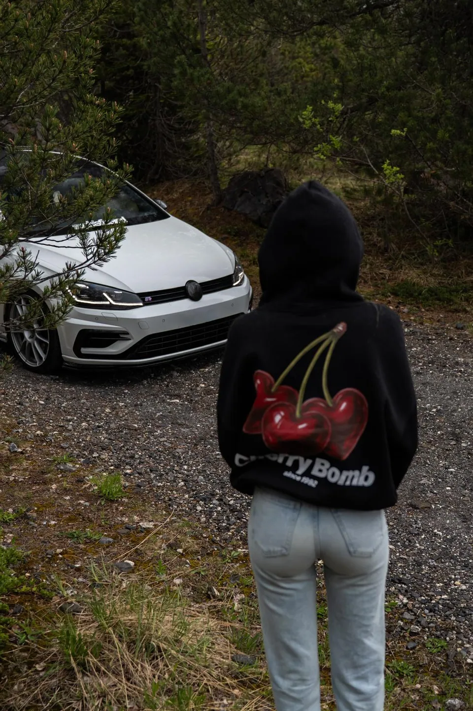 Personne de dos en sweat à capuche devant une Volkswagen Golf R blanche