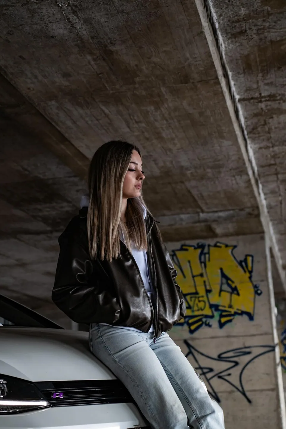 Personne assise sur le capot d'une Volkswagen Golf R blanche devant un mur taggé