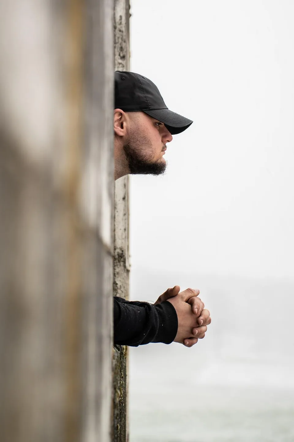 Profil d'un homme à casquette derrière un poteau de bois, décor hivernal